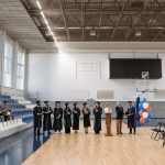 A graduation ceremony held in an indoor gymnasium with graduates and an audience.