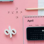 Flat lay of April calendar with calculator, pencil, and pink background for financial planning.