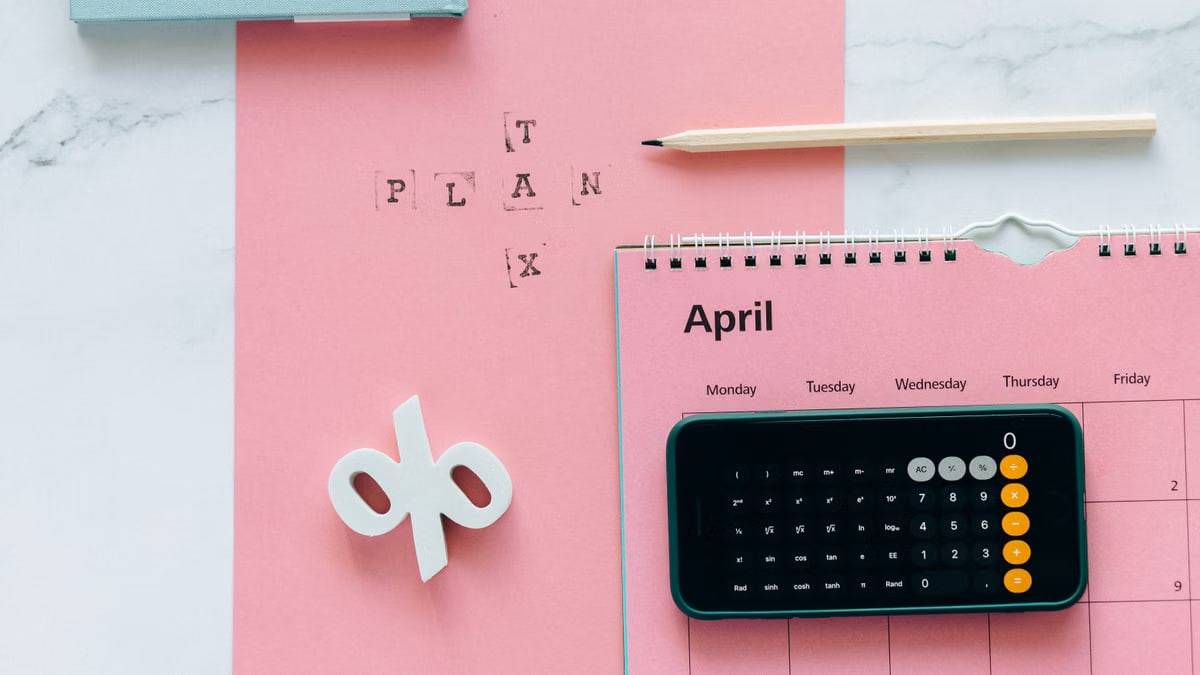 Flat lay of April calendar with calculator, pencil, and pink background for financial planning.